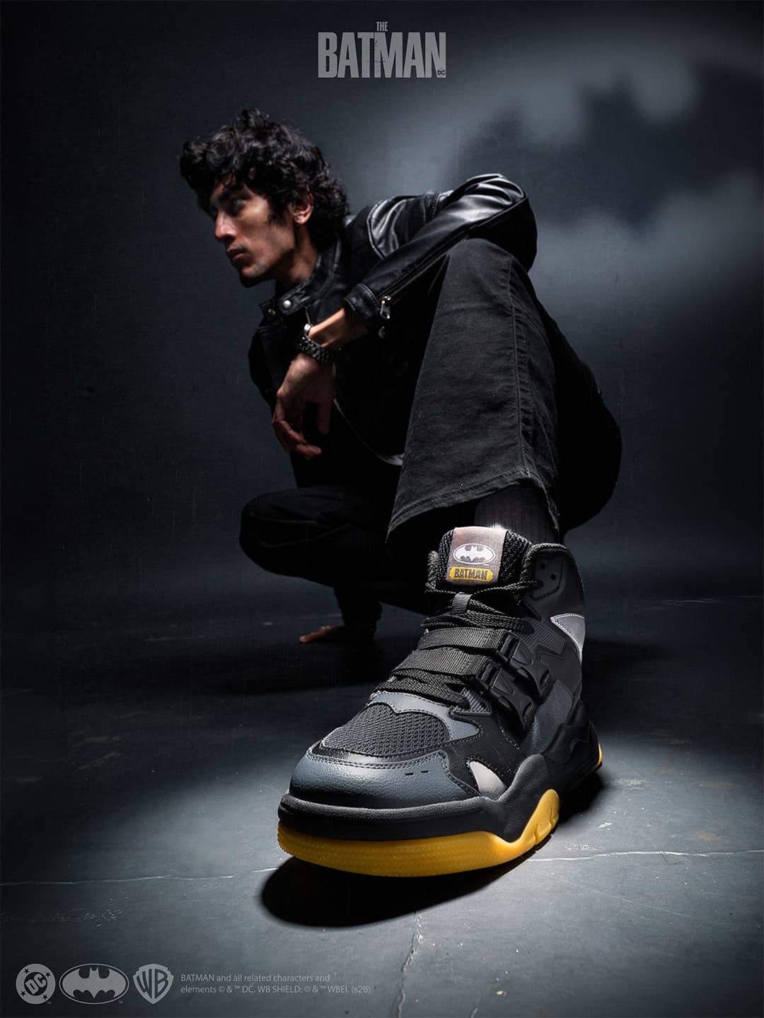Person wearing a black outfit with a high-top sneaker on a dark background, featuring the Batman logo.